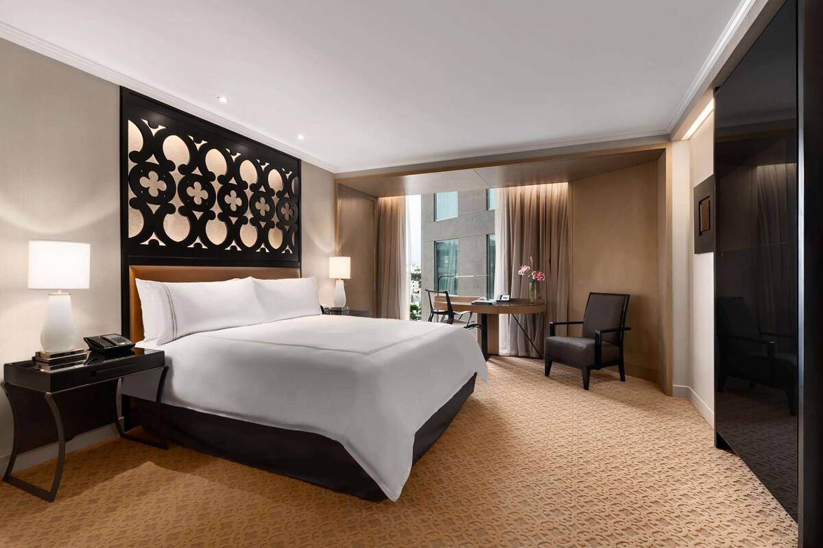 Ein Hotelzimmer mit einem großen Bett, einem Schreibtisch mit Stuhl, einem Spiegel und Blick auf die Stadt.