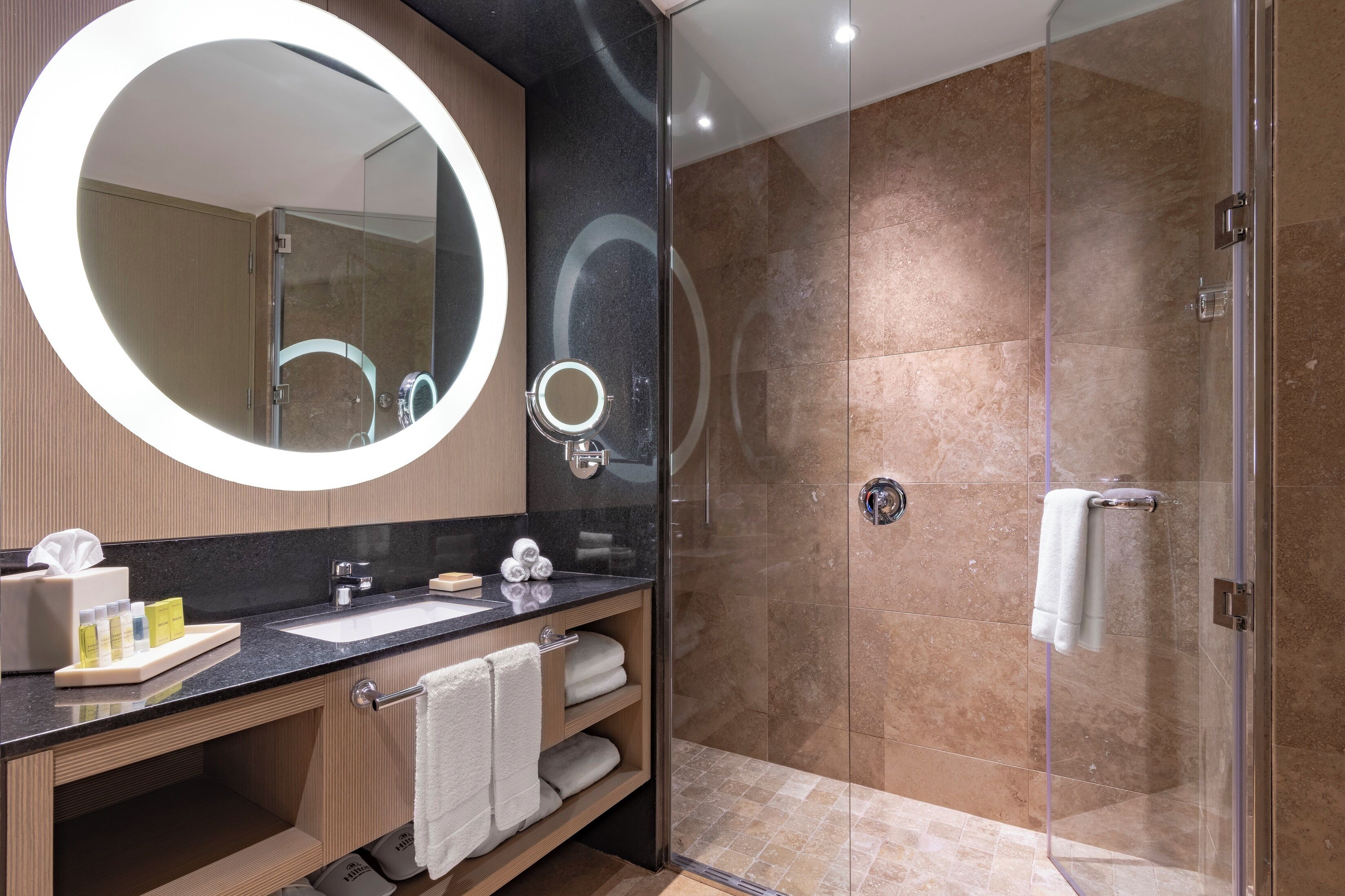 Un baño moderno con un espejo grande, un lavamanos y una ducha con mampara de vidrio.
