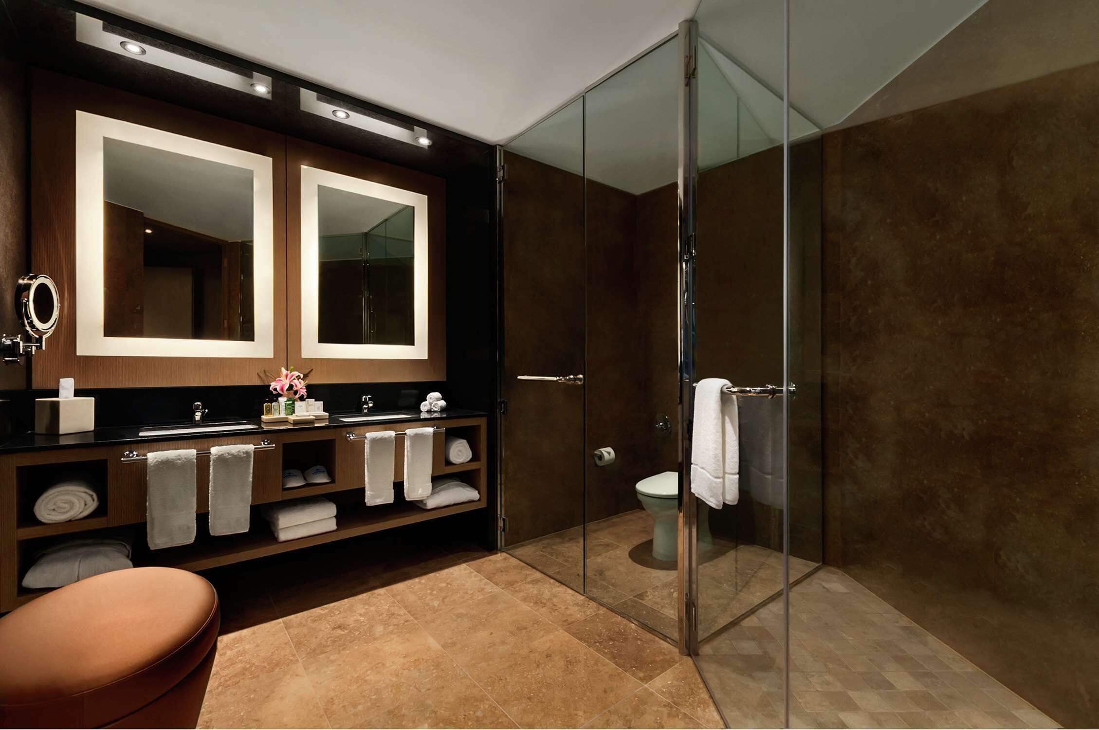 Un baño moderno con cabina de ducha de vidrio, un espejo grande y un tocador con varios toalleros.