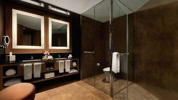 Un baño moderno con cabina de ducha de vidrio, un espejo grande y un tocador con varios toalleros.