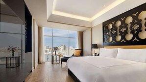 Una moderna camera d'albergo con un letto grande, vista sulla città, un pannello decorativo e un piccolo comodino con un vaso.