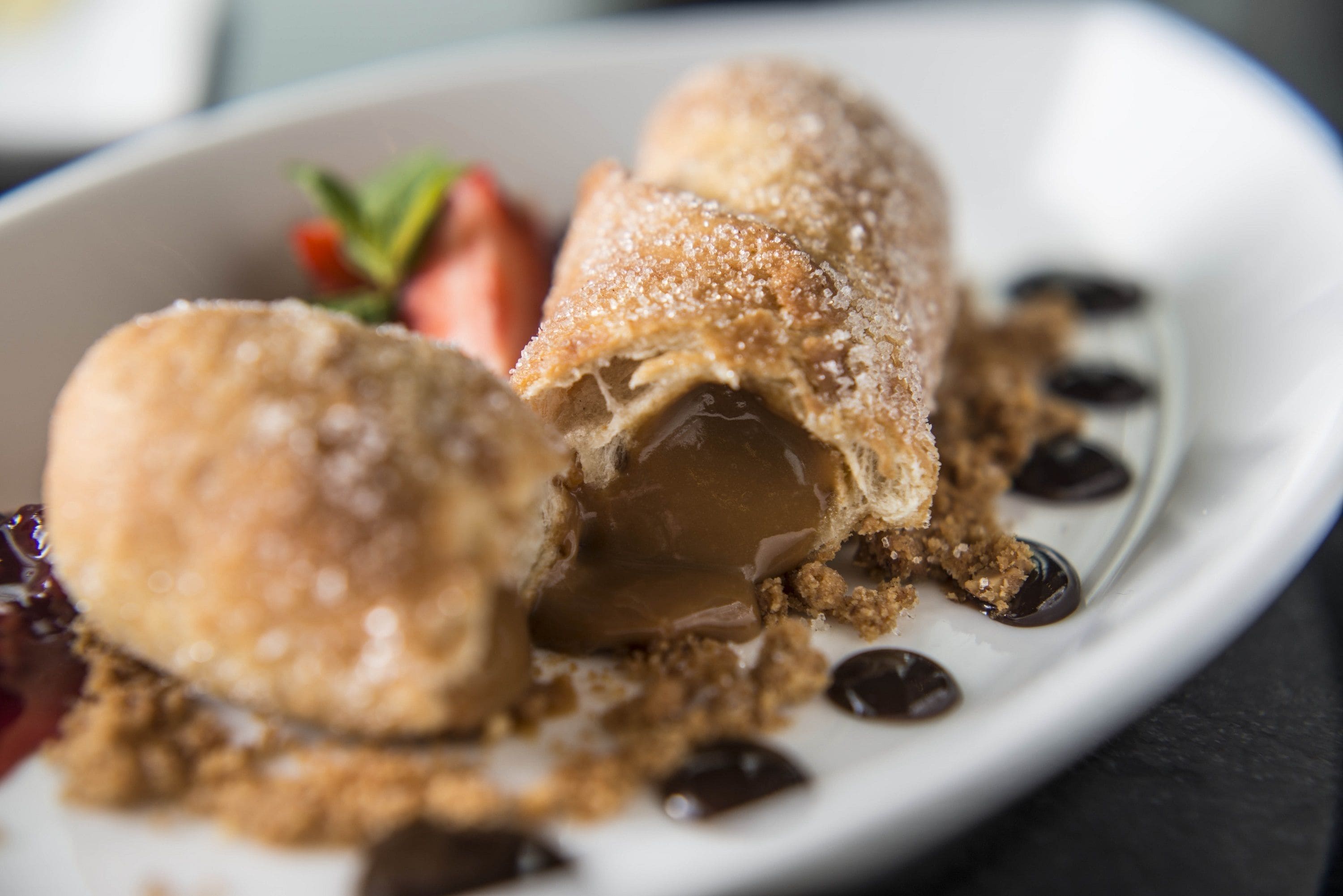 Un postre con centro de caramelo y exterior espolvoreado con azúcar, servido en un plato blanco con una decoración de fresa.