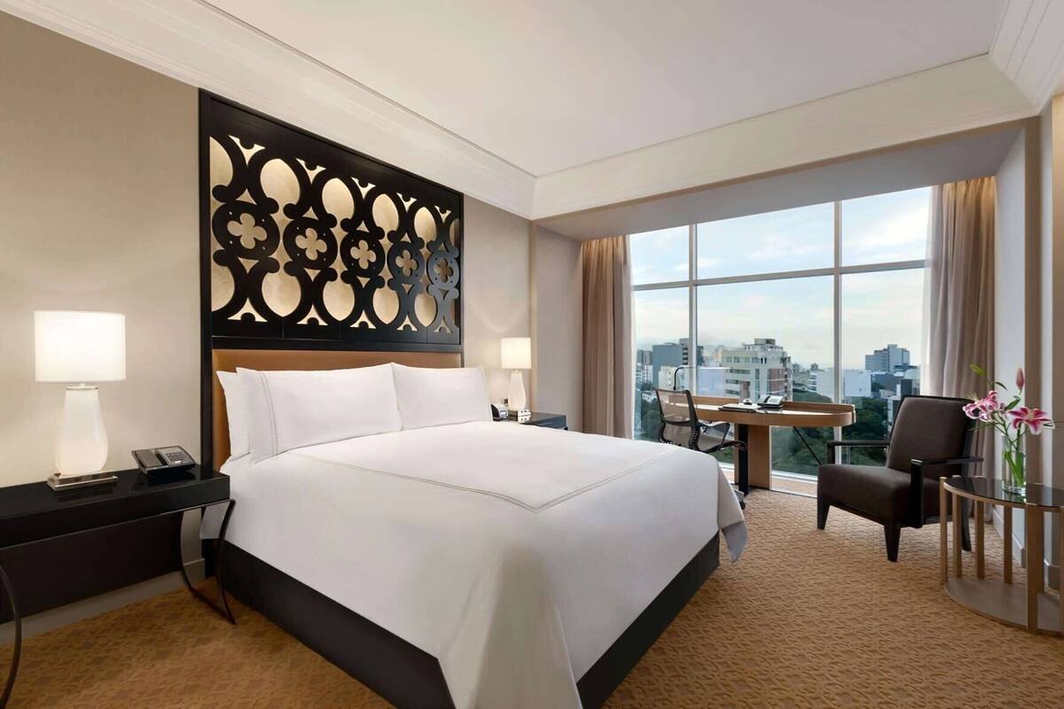 Ein Hotelzimmer mit einem großen Bett, einem Schreibtisch, einem Sessel und Blick auf die Stadt.