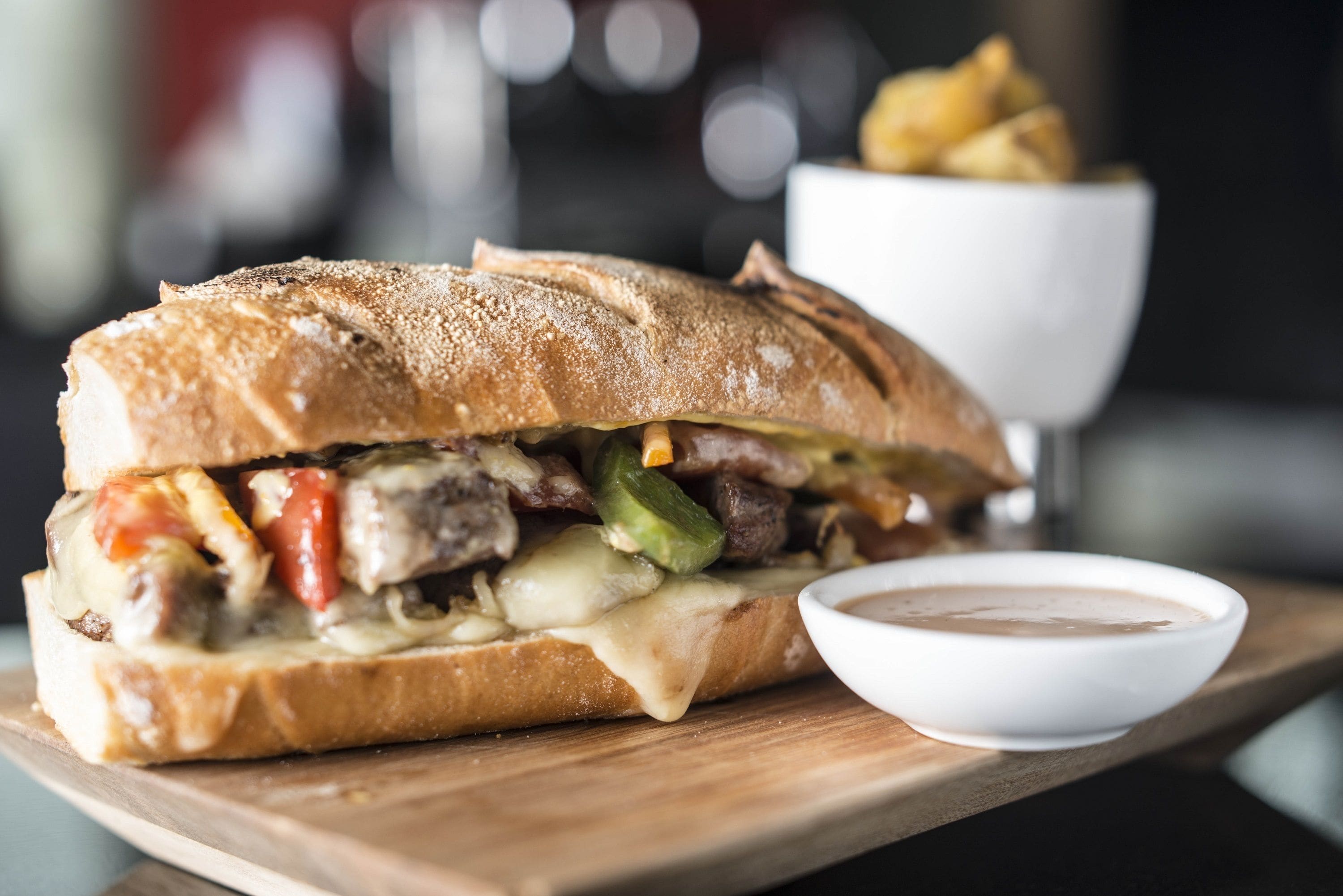 A sandwich with a side of dipping sauce and fries on a wooden board.