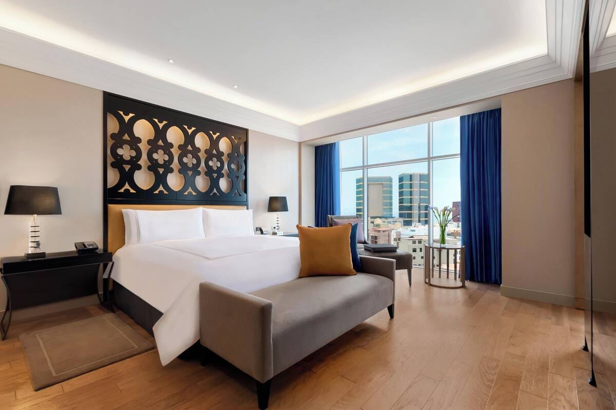 Ein modernes Hotelzimmer mit einem großen Bett, einer Sitzecke, einem Schreibtisch und Blick auf die Stadt.