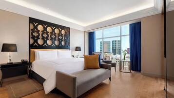 A modern hotel room with a large bed, a sofa, a desk, and a view of the city.