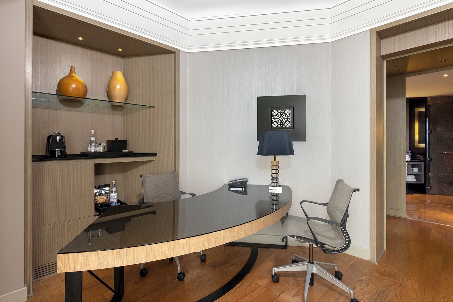 Una sala de conferencias con una mesa de vidrio, dos sillas, una máquina de café y una lámpara.