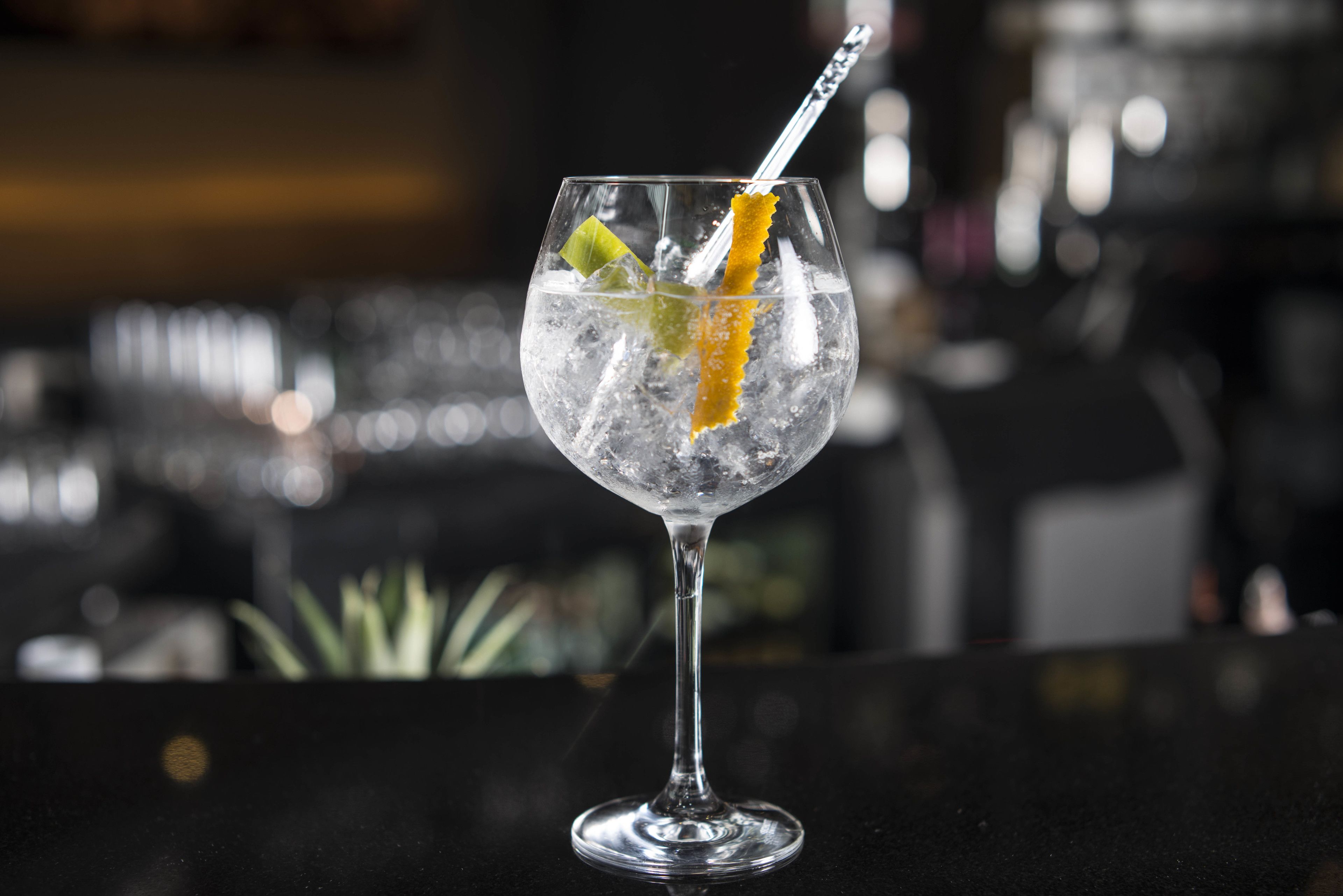 A cocktail glass with ice and a lemon slice on a bar counter.