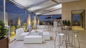 Una terrazza sul tetto con mobili bianchi, ringhiere in vetro e vista sulla città.