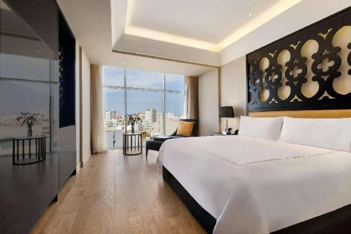 Ein modernes Hotelzimmer mit einem großen Bett, Blick auf die Stadt, einer dekorativen Wandverkleidung und einem kleinen Nachttisch mit einer Vase.