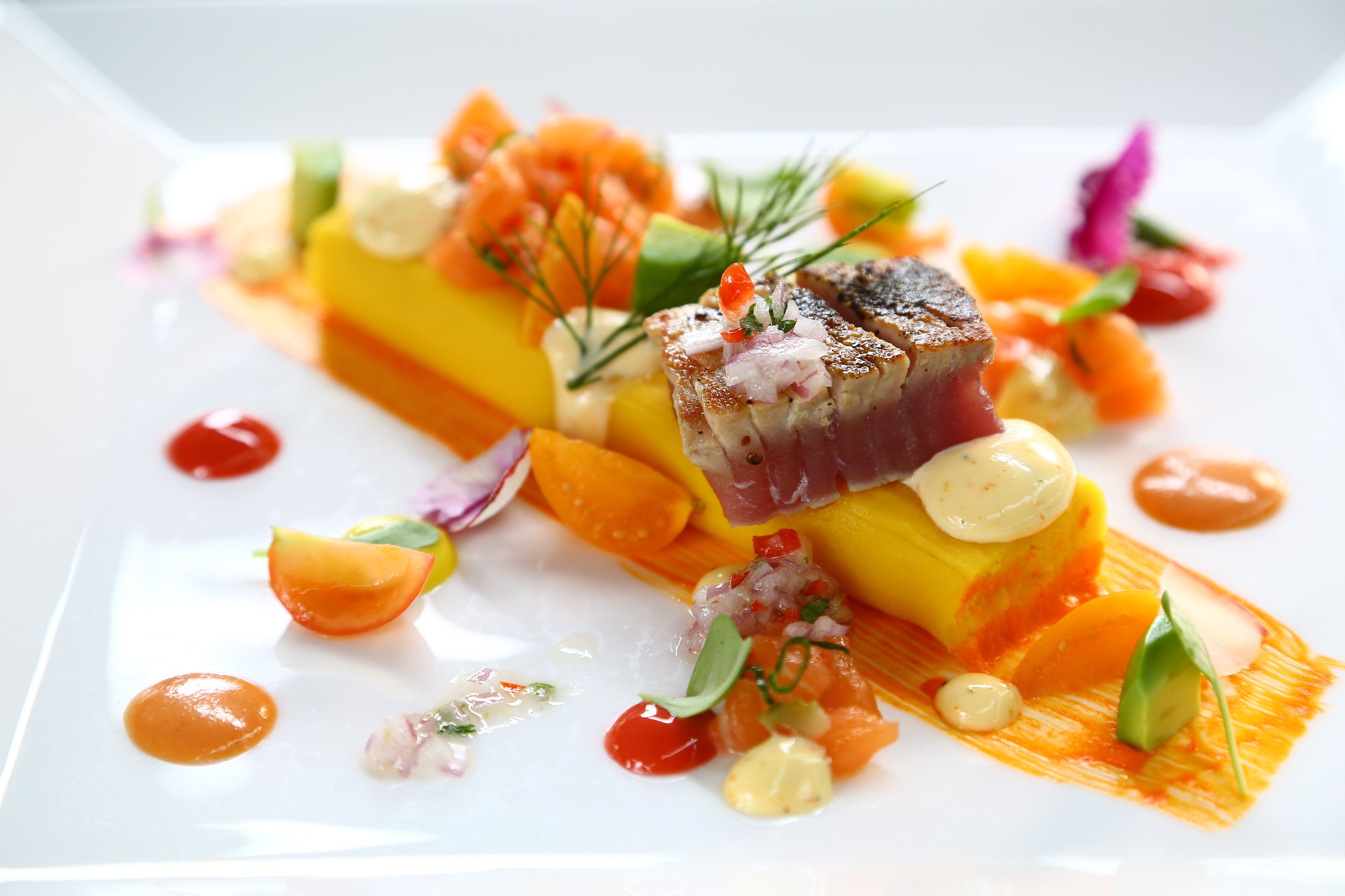 Un plato blanco con una variedad de alimentos, incluyendo pescado, verduras y salsas.