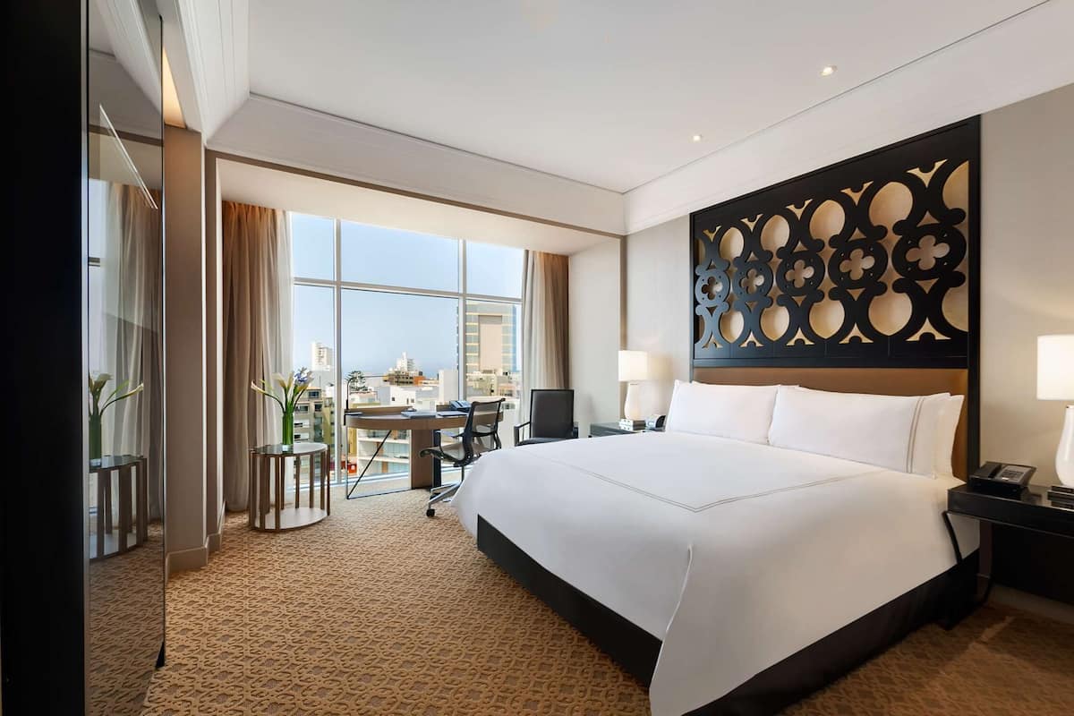 Ein Hotelzimmer mit einem großen Bett, einem Schreibtisch mit Stuhl, Blick auf die Stadt und einer Wandverkleidung.