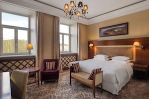 A hotel room with a large bed, a chair, a table, and a chandelier. - Grand Hotel Vilnius, Curio Collection by Hilton (Vilnius)