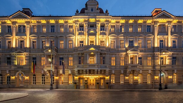 Un imposant bâtiment illuminé, doté d’une architecture classique, avec une entrée centrale et de nombreux balcons.