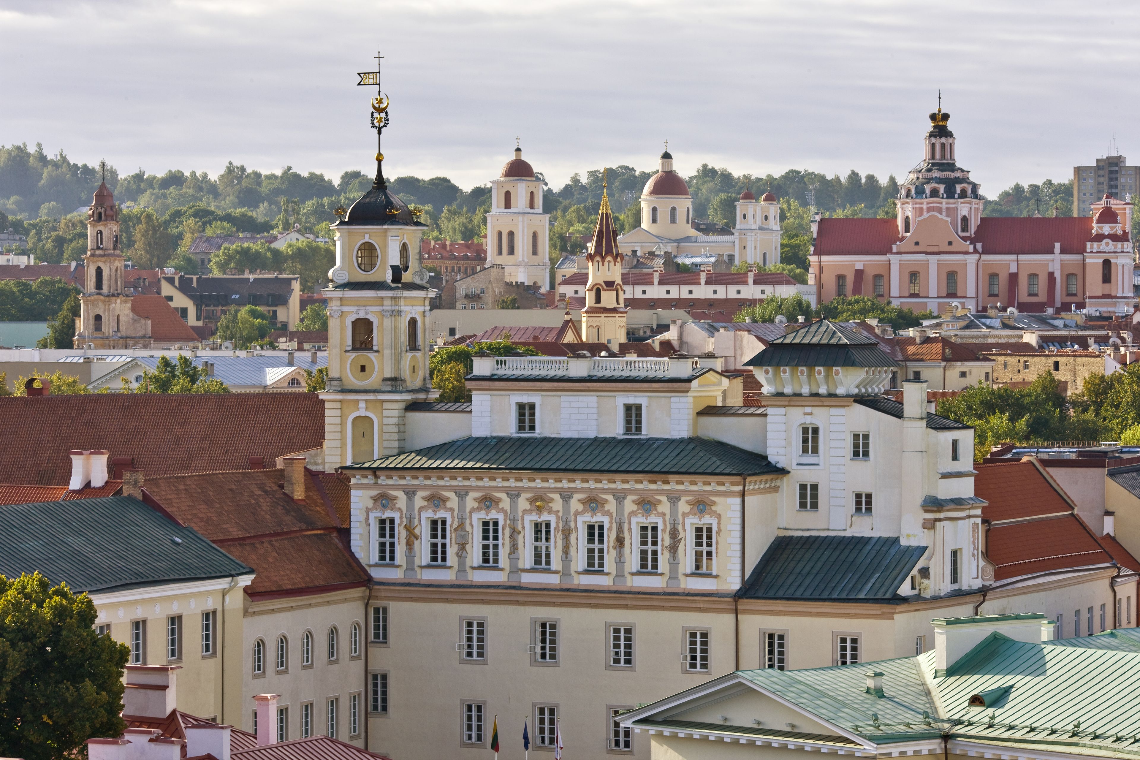 A historic building with classical architecture, featuring multiple domes and towers, surrounded by other buildings and a body of water.