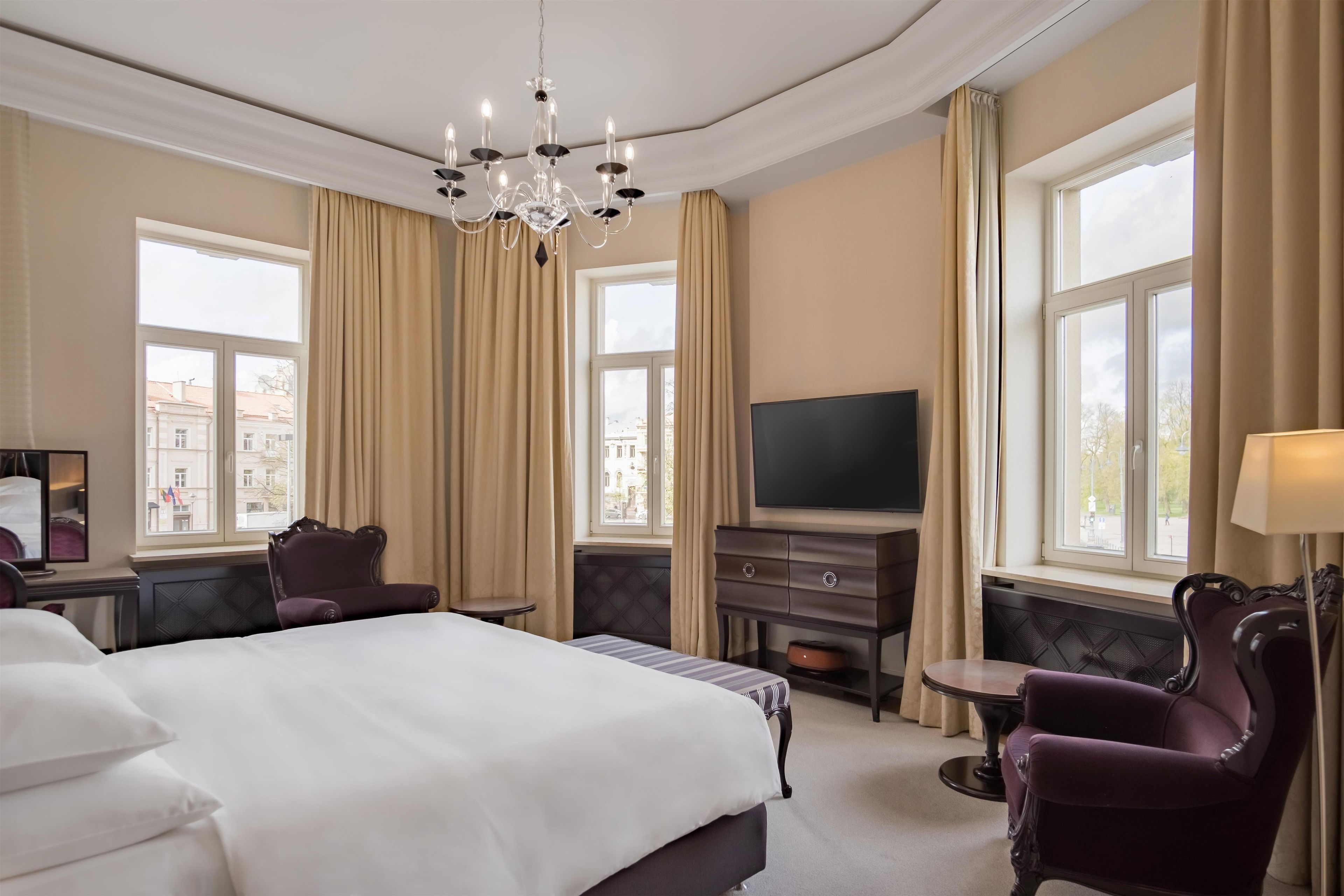 A hotel room with a large bed, a television, a desk, and a chair.