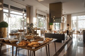 A spacious hotel lobby with a buffet table, large windows, and modern decor. - Grand Hotel Vilnius, Curio Collection by Hilton (Vilnius)