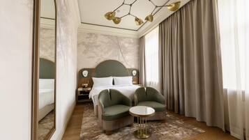 Une chambre d’hôtel avec un lit, deux fauteuils, une petite table ronde, un miroir et un lustre.