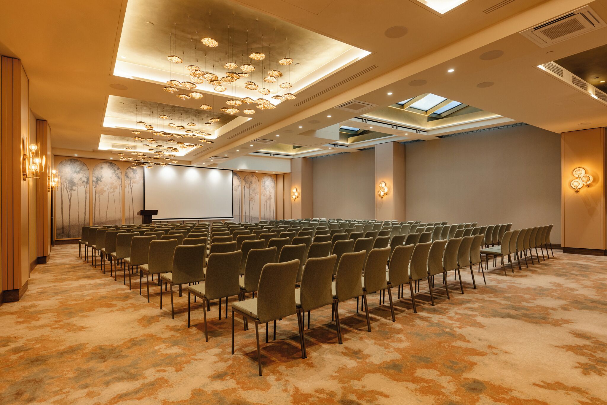 Una sala conferenze con file di sedie, un podio e un grande schermo.