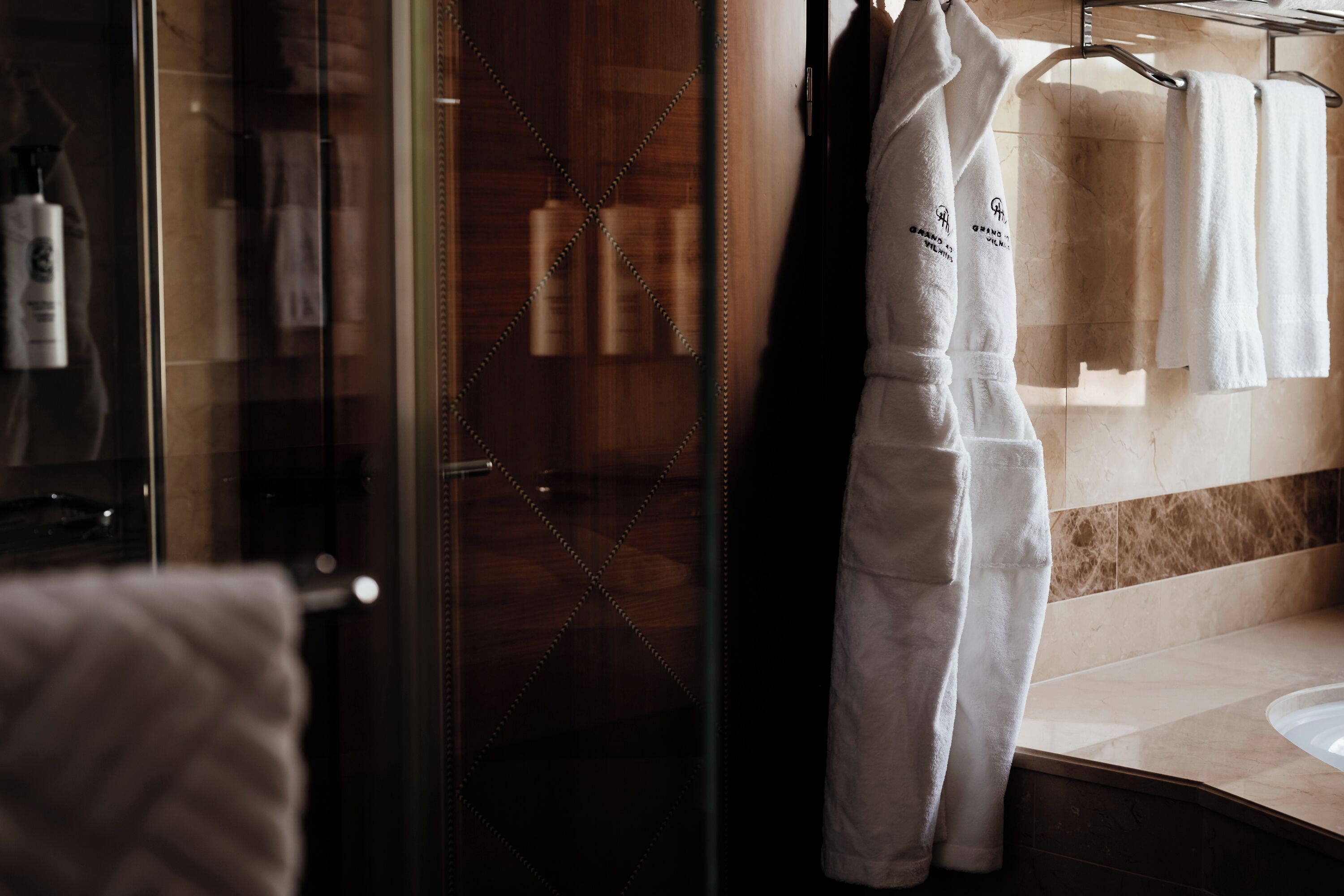 Un baño con puerta de vidrio para la ducha, un tocador de madera y toallas blancas colgadas en un perchero.