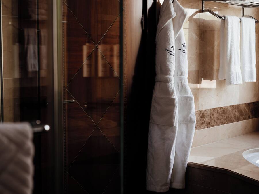 Un baño con puerta de vidrio para la ducha, un tocador de madera y toallas blancas colgadas en un perchero.