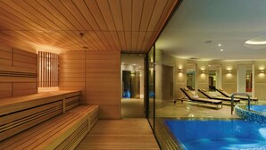 Un espace spa moderne avec des bancs en bois, une piscine entourée de parois en verre et des chaises longues.