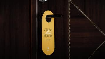 Une porte d’hôtel avec une poignée dorée et une pancarte sur laquelle on peut lire : « EN ROUTE POUR MARQUER L’HISTOIRE » et « VEUILLEZ NETTOYER MA CHAMBRE ».