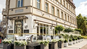 L’extérieur d’un hôtel, avec une terrasse, une façade en verre et une clôture décorative agrémentée de fleurs.
