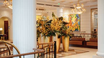 A lobby with a grand staircase, large golden planters with yellow flowers, and a colorful abstract painting on the wall.