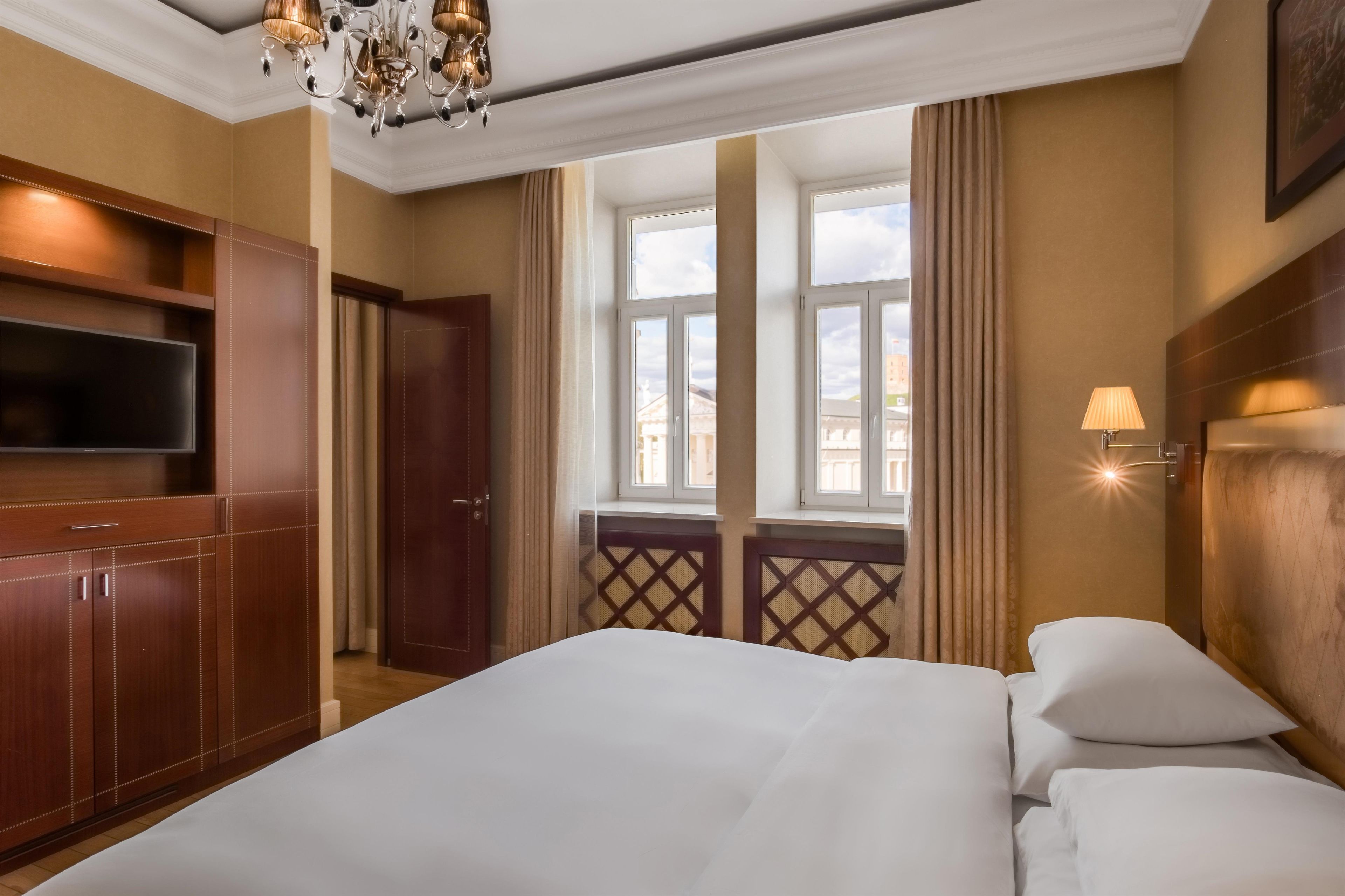 Ein Hotelzimmer mit einem großen Bett, einem an der Wand montierten Fernseher und einem Fenster mit Vorhängen.