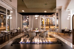 Un restaurante con mesas redondas, sillas y una chimenea central.