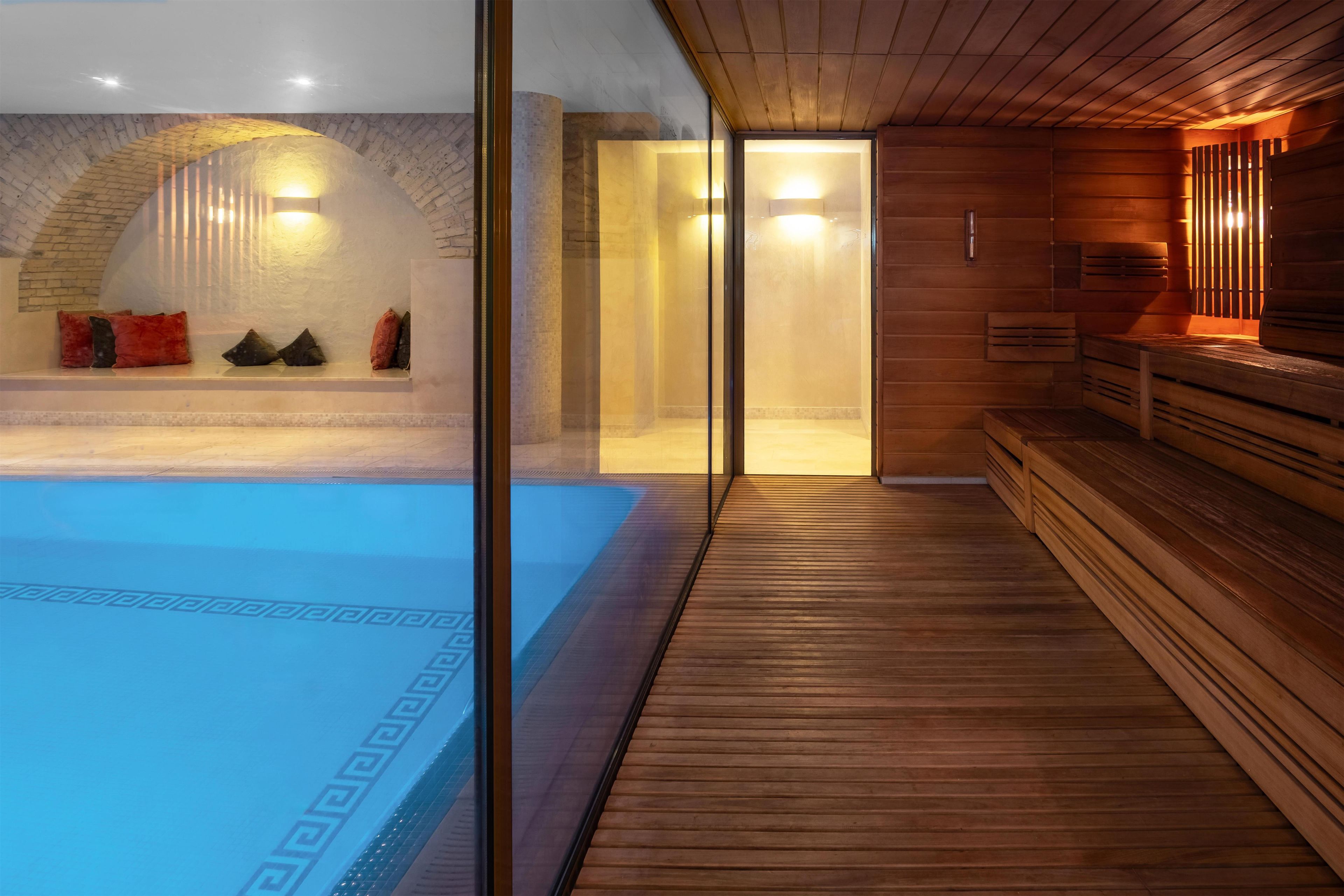 Una sala de sauna con un banco de madera, un muro de vidrio y una zona de piscina visible a través del vidrio.