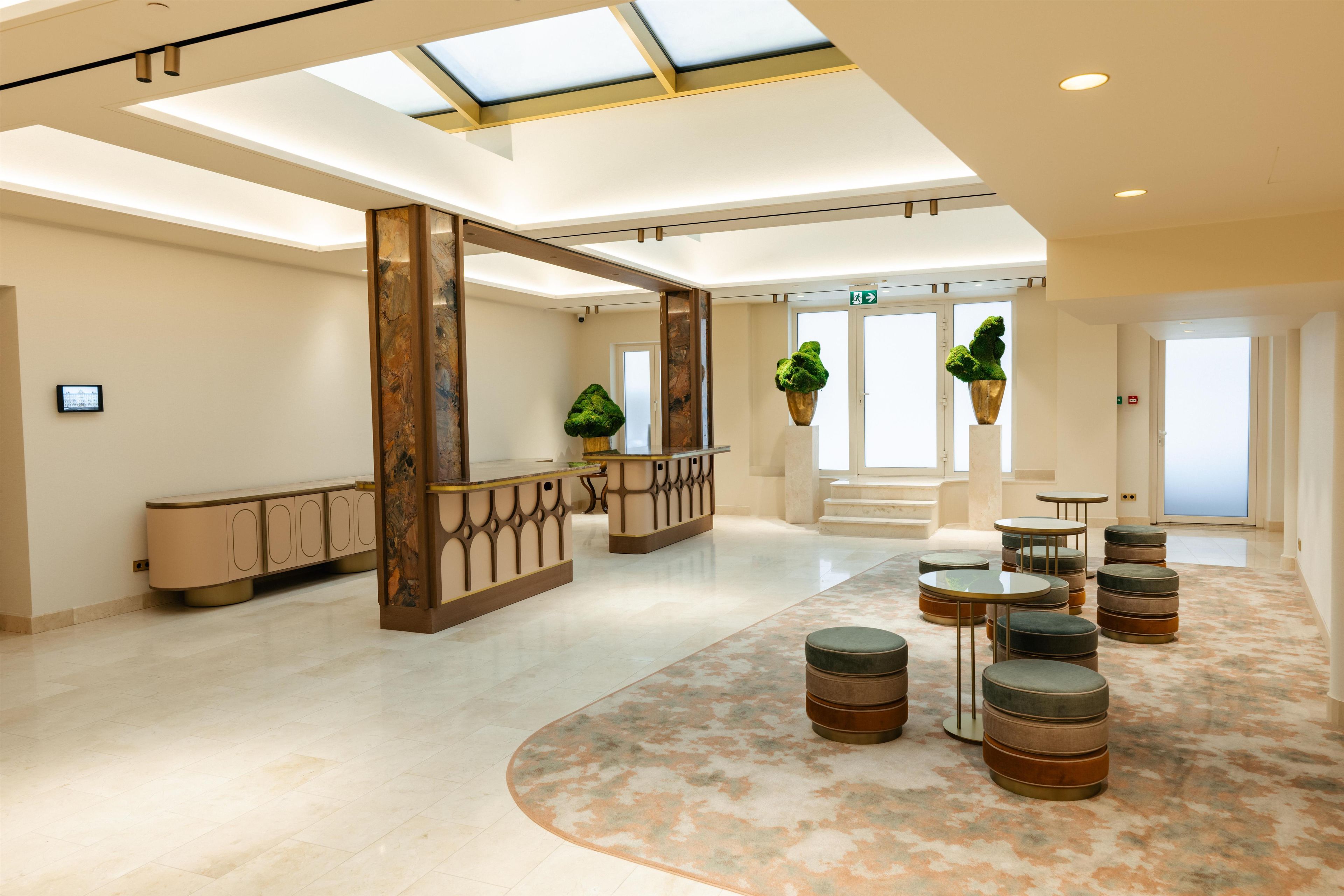 Een ruime lobby met een hoge plafond, een centraal receptiegedeelte en een zithoek met ronde tafels en krukjes.