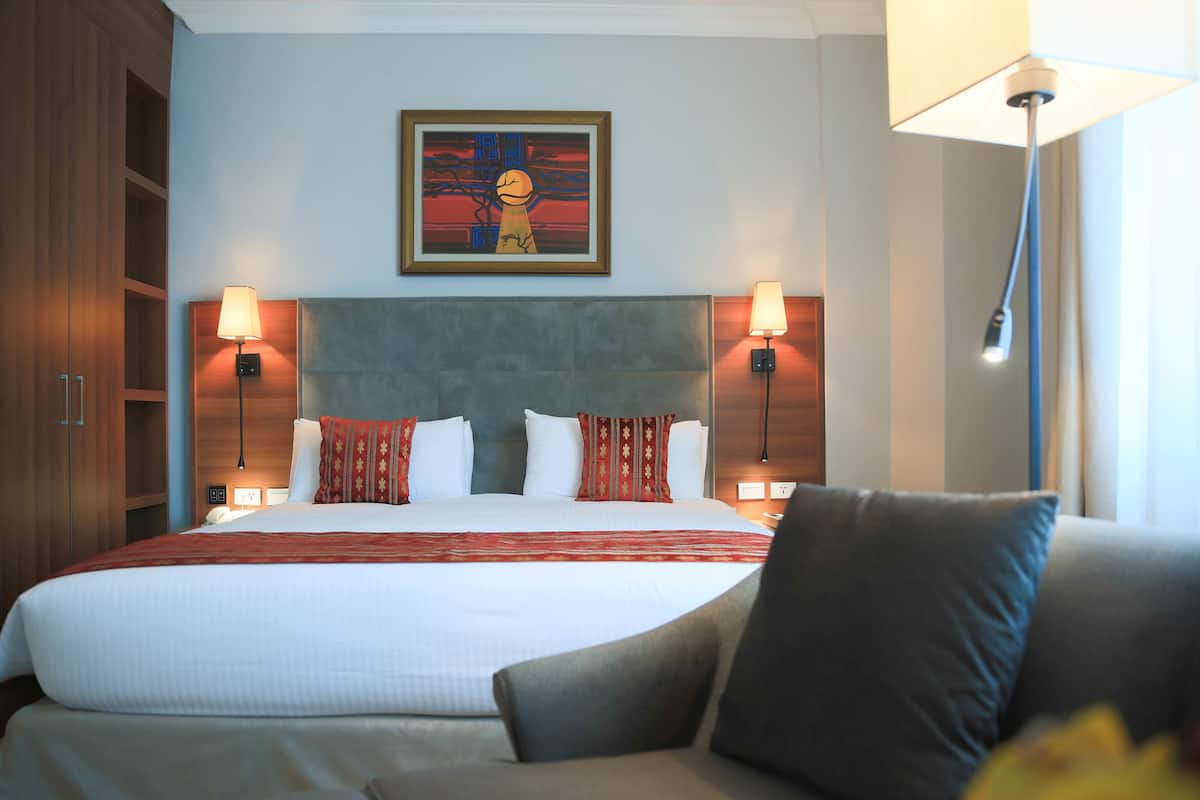 A hotel room with a large bed, two bedside lamps, a headboard, and a painting on the wall.