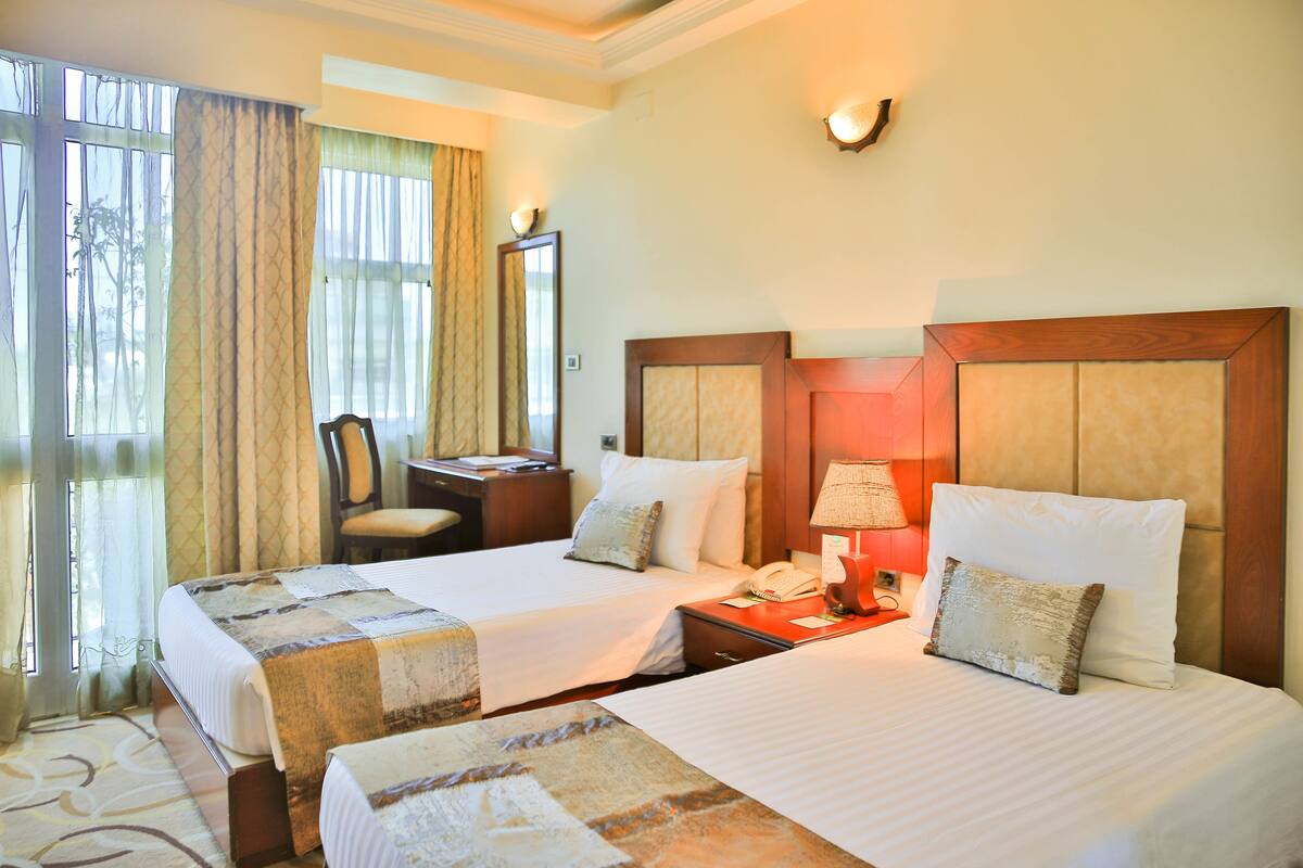 A hotel room with two beds, a desk, a chair, and a lamp.