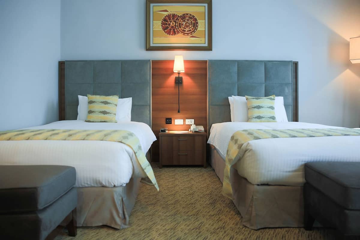 A hotel room with two beds, a nightstand, a lamp, and a framed picture on the wall.