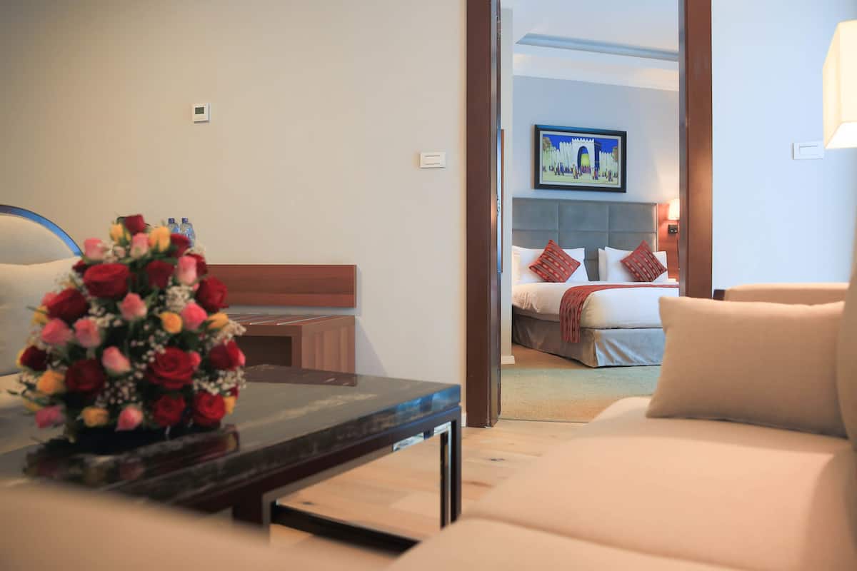 A hotel room with a bed, a desk with a vase of flowers, a sofa, and a painting on the wall.