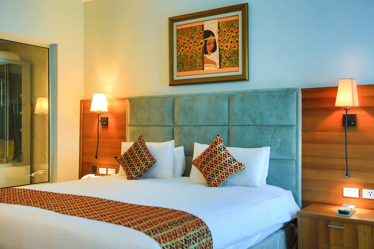 A hotel room with a large bed, two bedside lamps, a headboard, and a framed artwork on the wall.