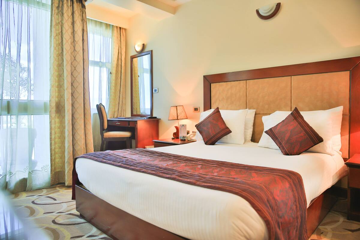 A hotel room with a large bed, a desk, a chair, and a mirror.