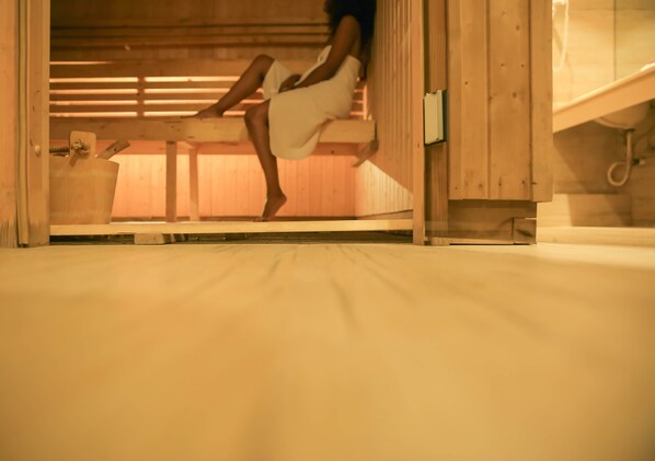 A person sitting on a wooden bench in a room with a wooden ceiling and a bed with a white mattress.