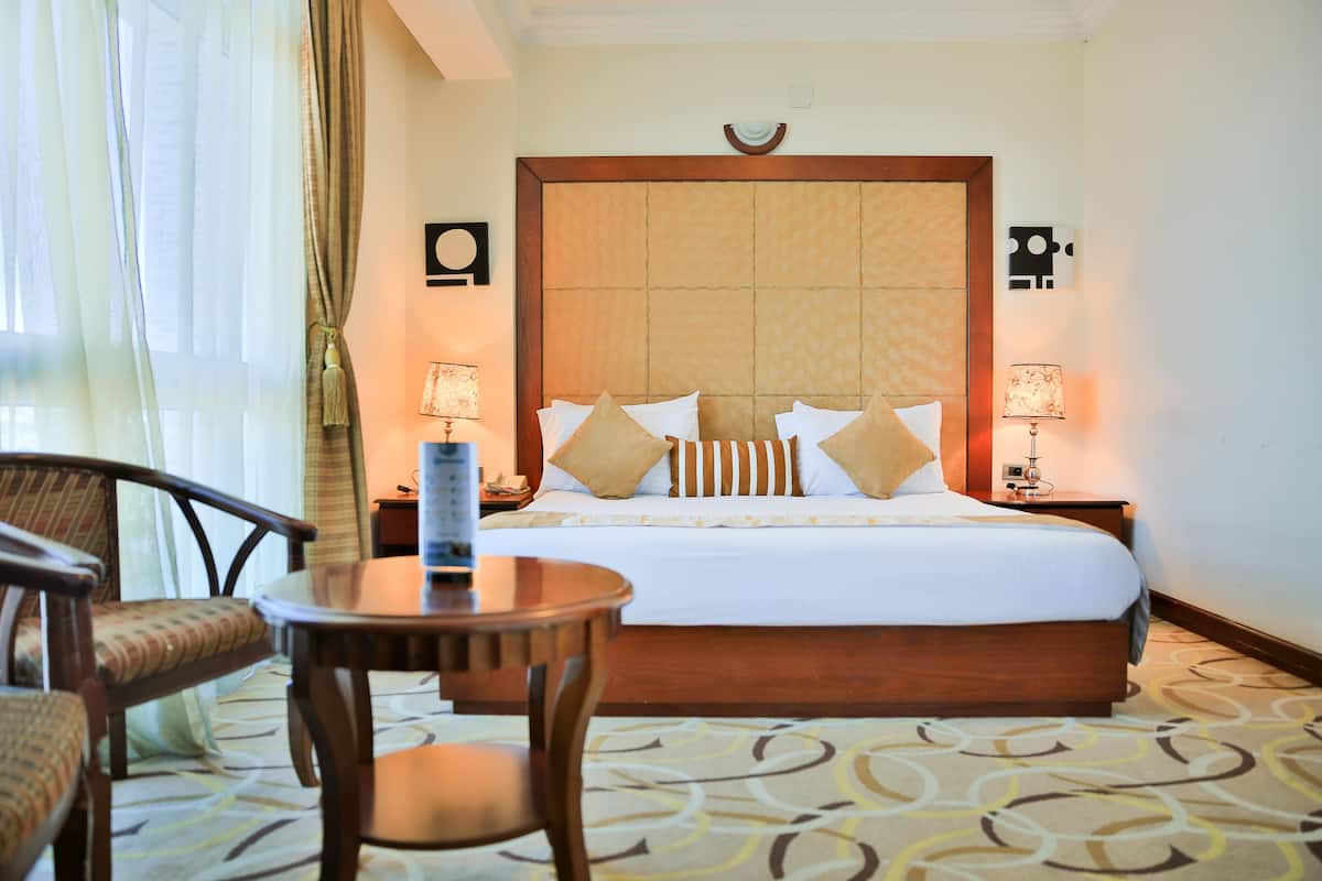 A hotel room with a large bed, two bedside tables with lamps, a round table, and two chairs.