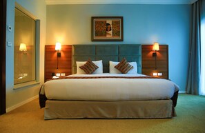 A hotel room with a large bed, two bedside lamps, a headboard with a picture, and a window with a view.