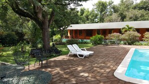 Un espace piscine avec des chaises longues, une terrasse en briques et un bâtiment doté d’un toit végétalisé.