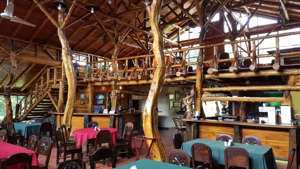 Un intérieur rustique en bois, avec de hauts plafonds et des poutres apparentes, comprenant un espace d’accueil et plusieurs tables à manger.