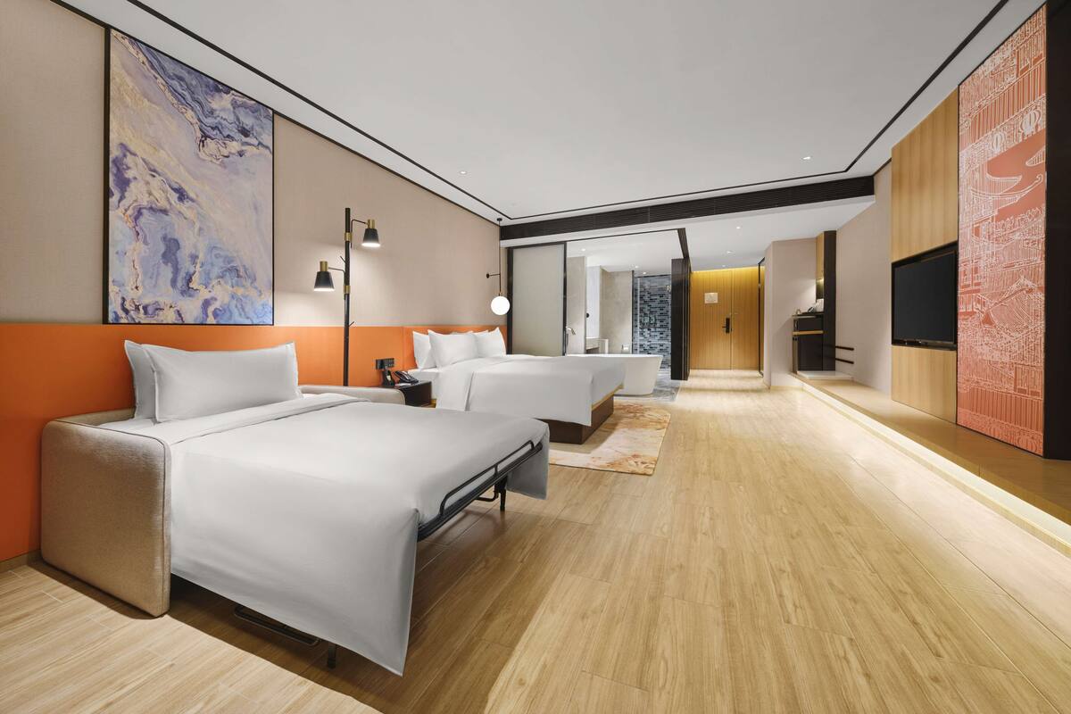 A modern hotel room with two beds, a large abstract painting, a wooden floor, and a TV mounted on the wall.