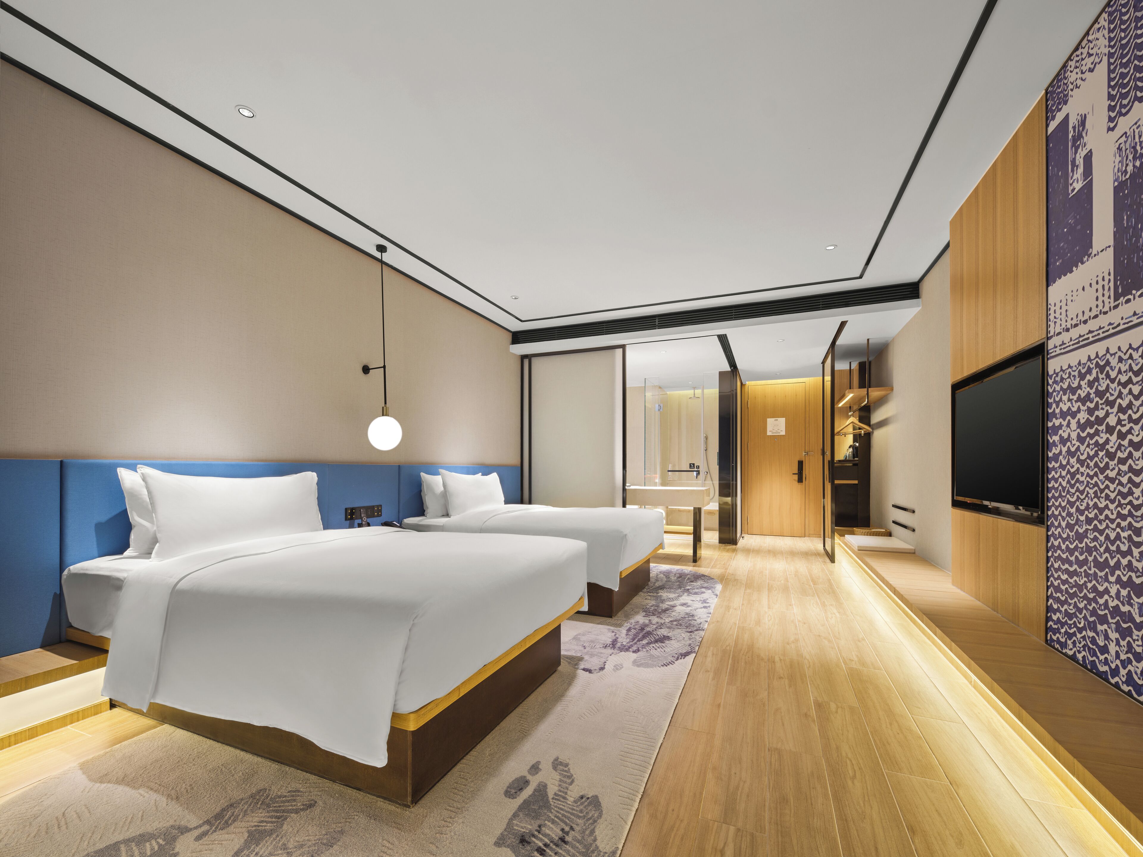 A modern hotel room with two beds, a large mirror, a TV, and a bathroom visible through a glass door.