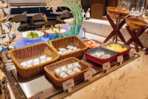 A buffet with various food items and condiments, including baskets of cheese and bowls of fruit.