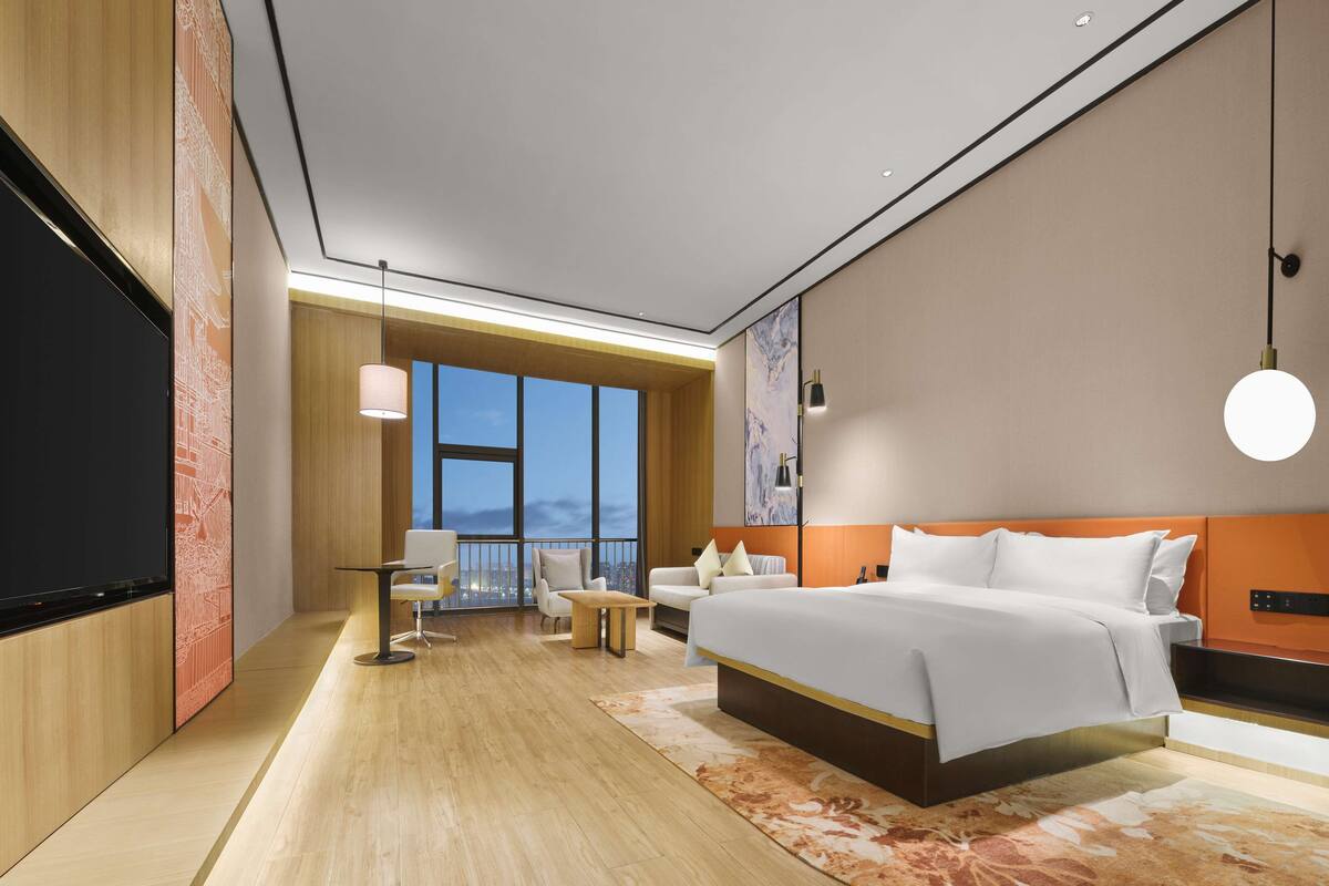 A modern hotel room with a large bed, a desk, and a TV.