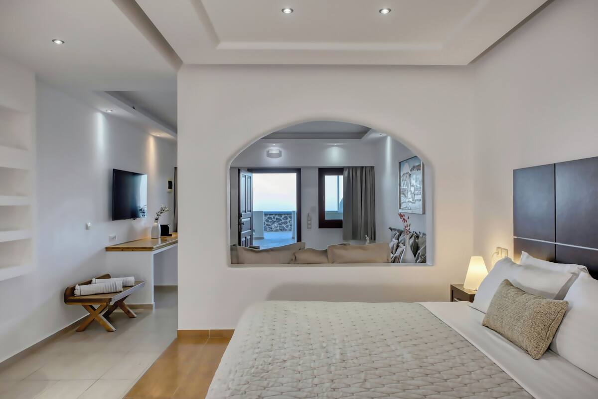 Une chambre d’hôtel moderne avec un grand lit, un téléviseur fixé au mur, un petit bureau et une vue sur l’extérieur grâce à une grande fenêtre.