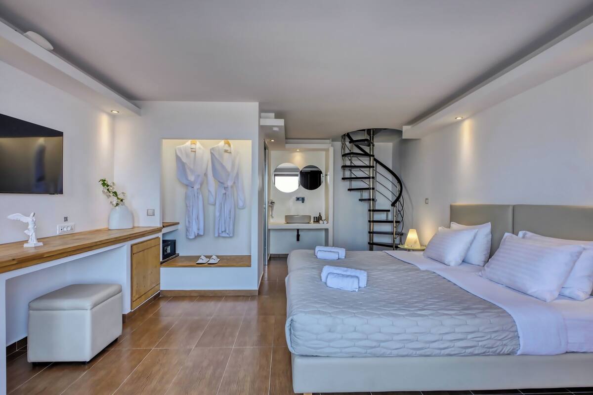 Une chambre d’hôtel moderne comprenant un lit, un bureau, une chaise, un miroir, un miroir rond, un escalier en colimaçon noir et une petite salle de bain.
